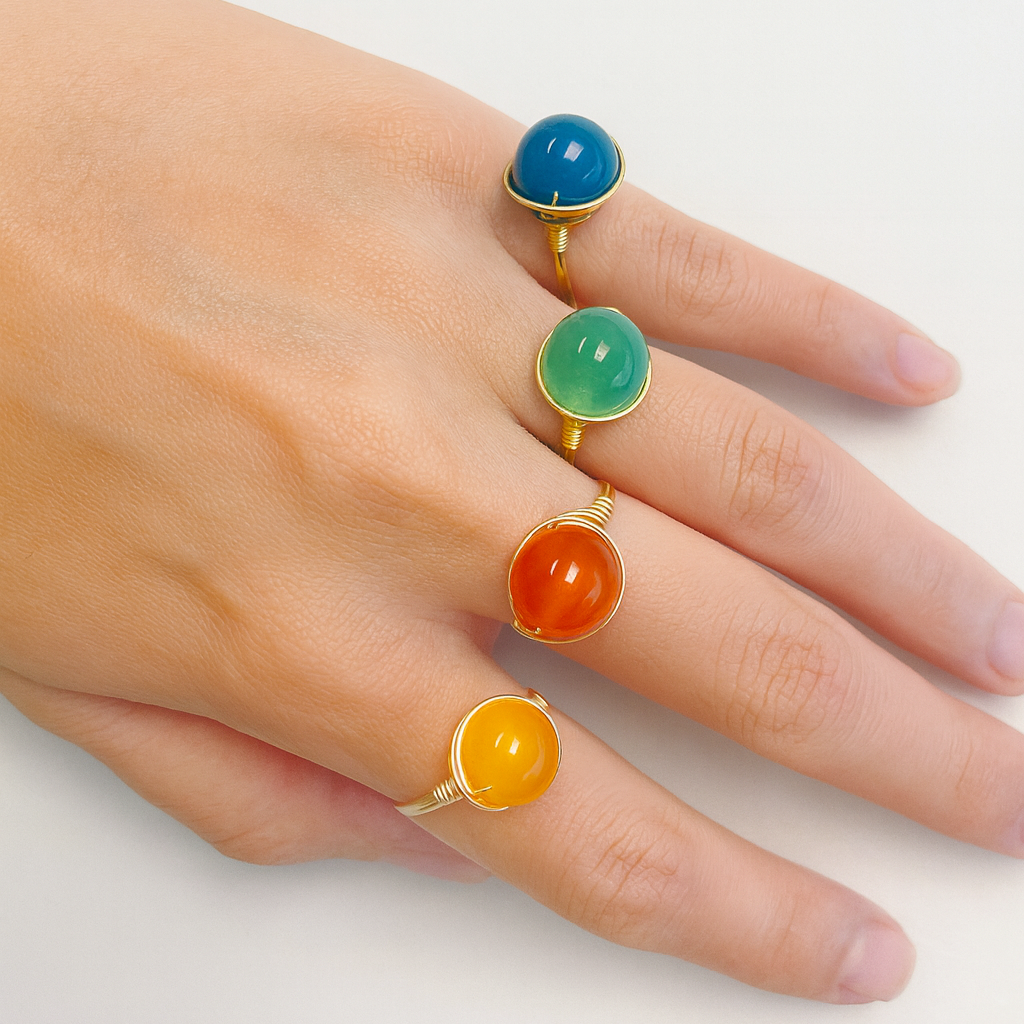 Hand wearing four colorful gemstone rings on a white background